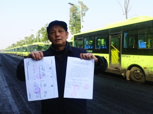 劉明手持多個部門的審批文件，身后就是閑置在路邊的電動公交車
